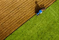 An aerial view of a tractor plowing a lush, green field